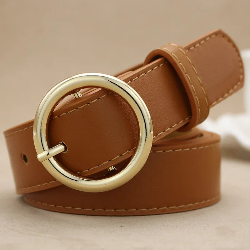 Brown leather belt with round gold buckle and visible stitching, rolled up on beige background