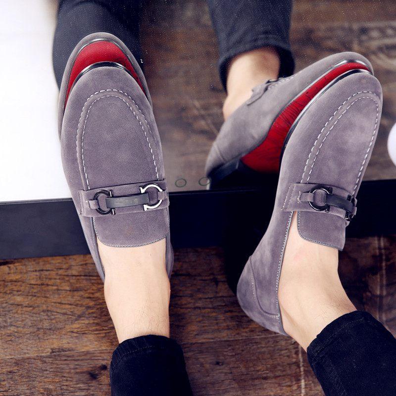 Grey suede men's loafers with black metal buckle and red soles worn on wooden floor