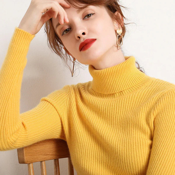 Woman in yellow ribbed turtleneck sweater with red lipstick and gold earrings sitting on wooden chair