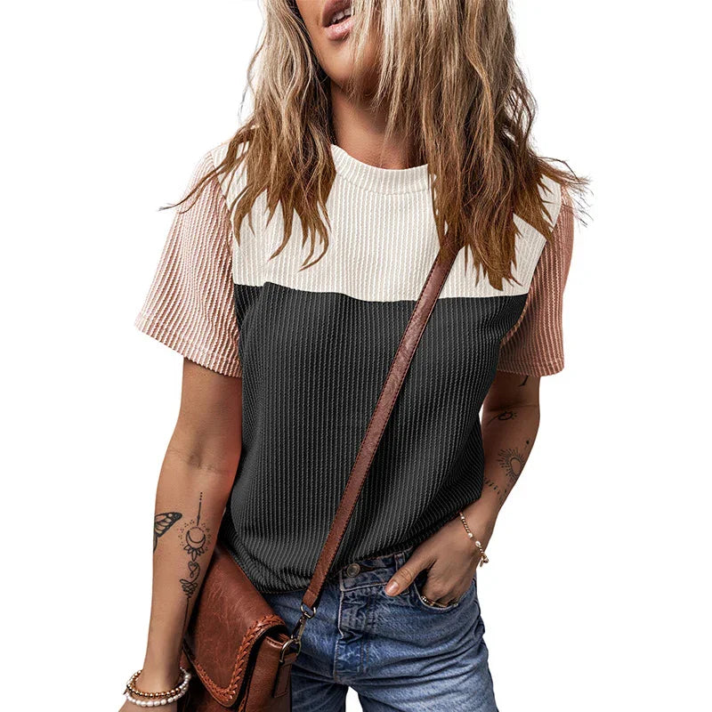 Woman wearing a color-block ribbed knit t-shirt with pink, white, and black sections, paired with blue jeans and a brown leather crossbody bag