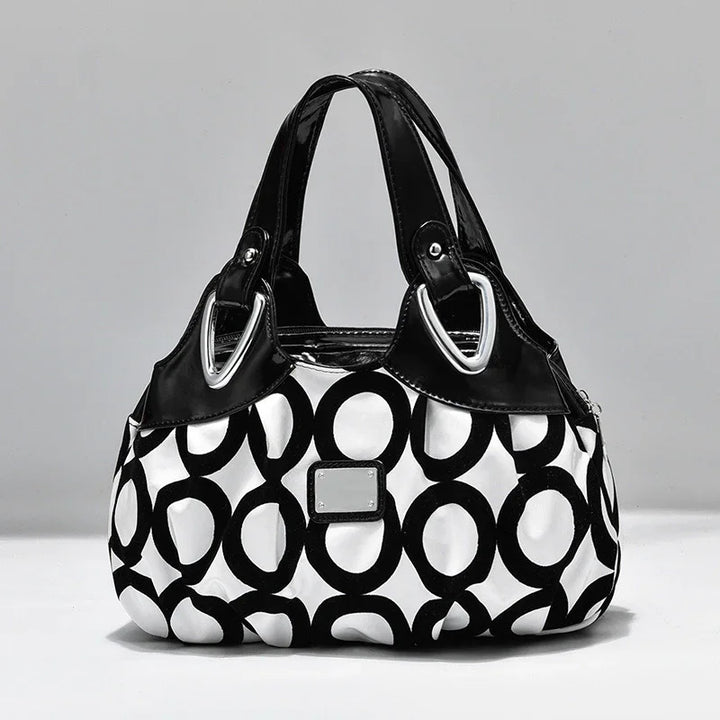 Black and white handbag with circular pattern and black patent leather handles on gray background