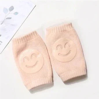 Pair of beige baby knee pads with smiling face design on a white surface