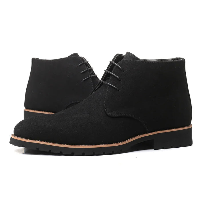 Black suede chukka boots with lace-up design and brown sole on white background