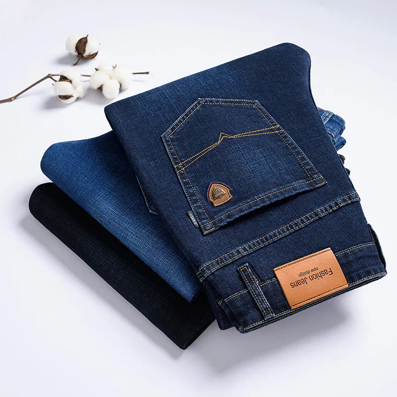 Stack of folded blue denim jeans with fashion jeans label and cotton branch on white background