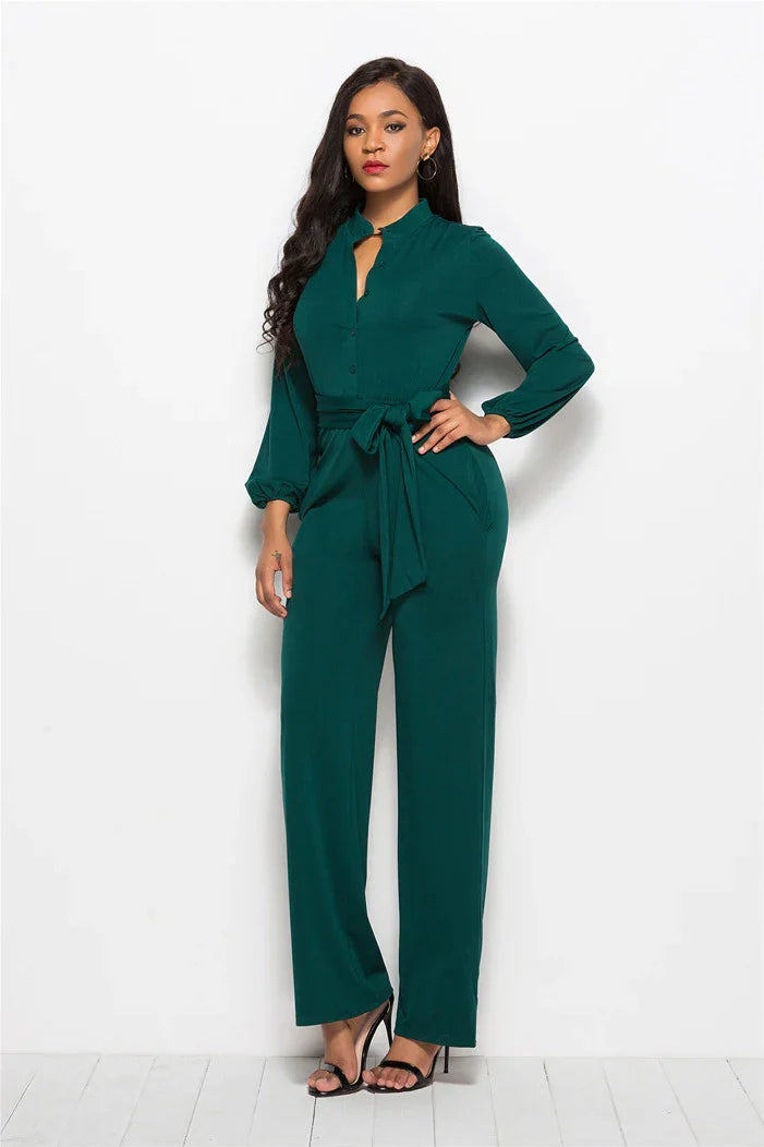 Elegant woman wearing a dark green button-up jumpsuit with long sleeves and waist tie, posing against white background