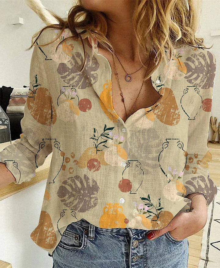 Woman wearing beige button-up blouse with abstract leaf and vase print paired with blue jeans indoors