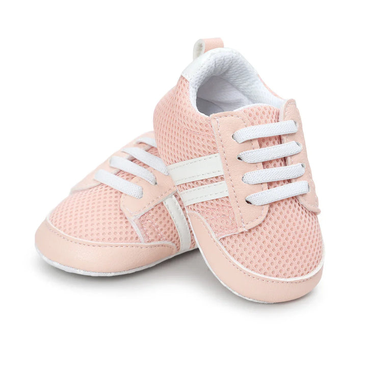 Pair of soft pink baby sneakers with white mesh and white elastic laces on white background