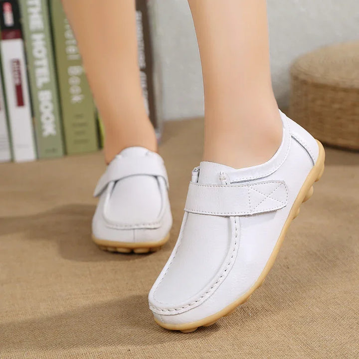 White casual slip-on shoes with velcro strap and beige sole worn indoors on carpet