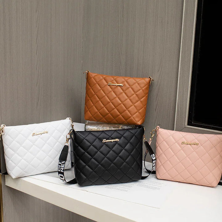 Four quilted crossbody bags in brown, white, black, and pink displayed on a white surface against a wood panel background