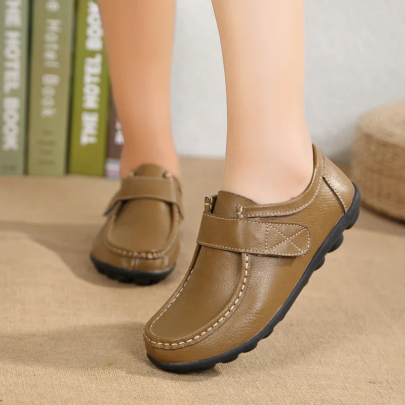 Brown leather casual shoes with black rubber soles worn indoors on beige floor