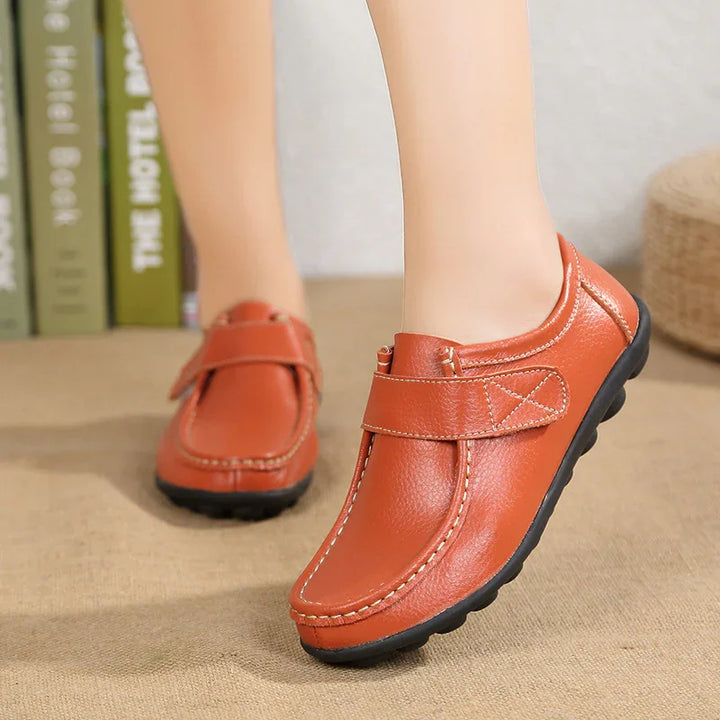brown leather casual shoes with black soles and Velcro straps on feet indoors