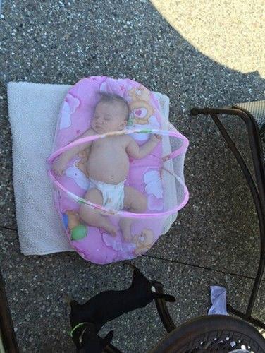 Sleeping baby in a diaper on a pink cushion with teddy bear prints outdoors on a textured ground