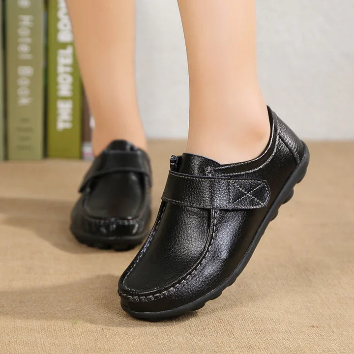 Black leather casual shoes with adjustable strap worn indoors on carpeted floor