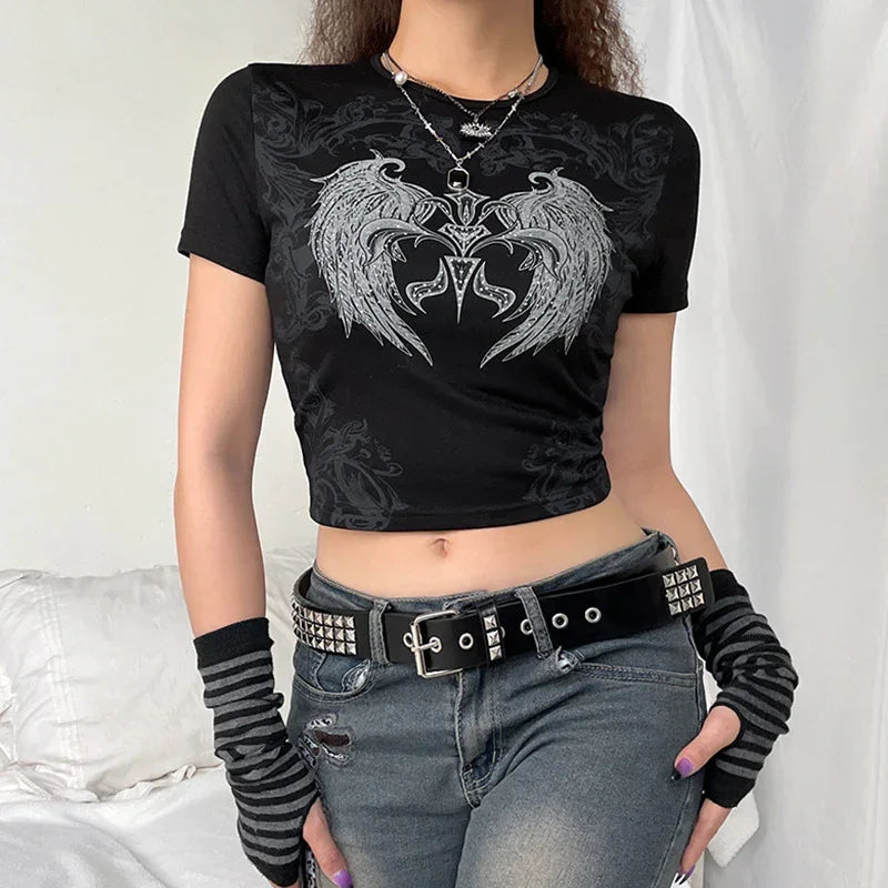 Person wearing black crop top with grey dragon wings graphic, studded belt, striped fingerless gloves, and jeans