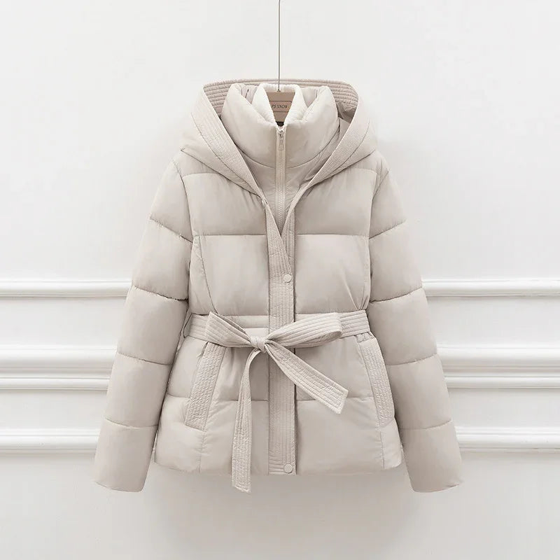 Beige padded winter jacket with belted waist and hood, hanging on white wall