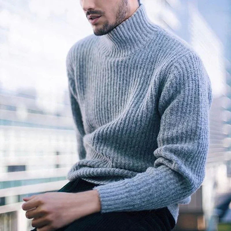 Man wearing soft gray ribbed turtleneck sweater sitting outdoors with blurred background