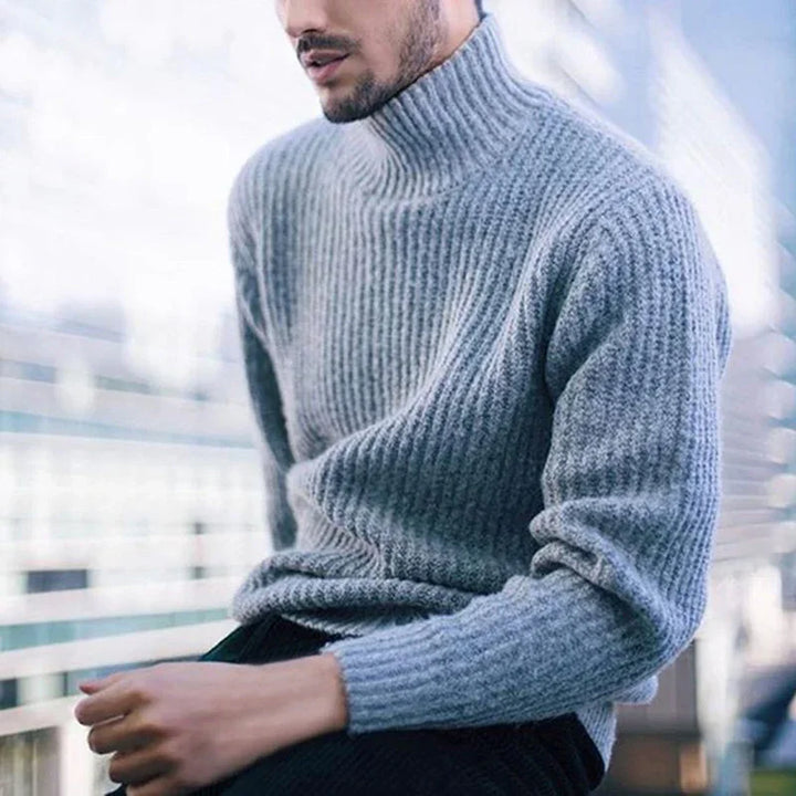 Man wearing soft gray ribbed turtleneck sweater sitting outdoors with blurred background
