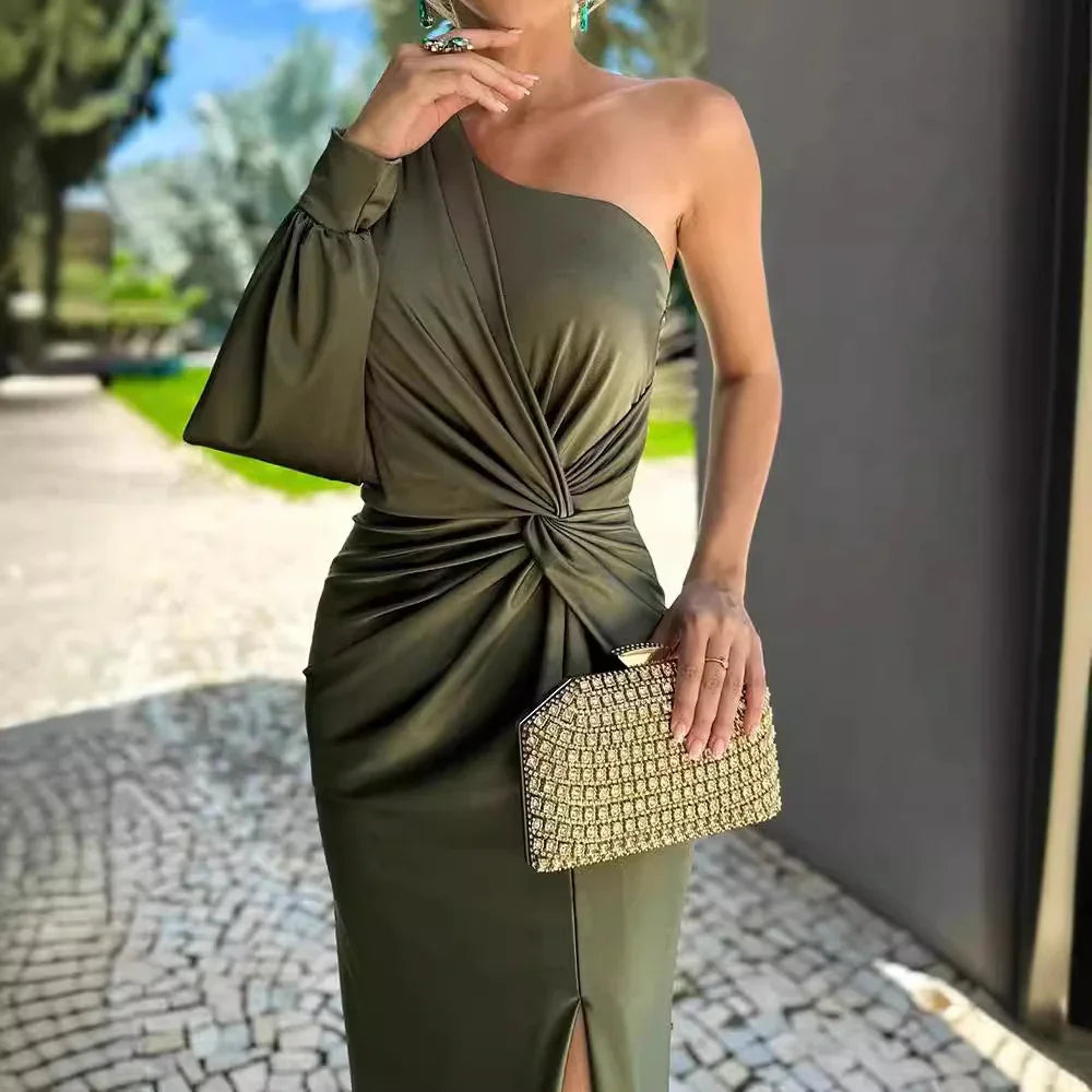 Woman in elegant olive green one-shoulder dress with draped detail holding a gold beaded clutch