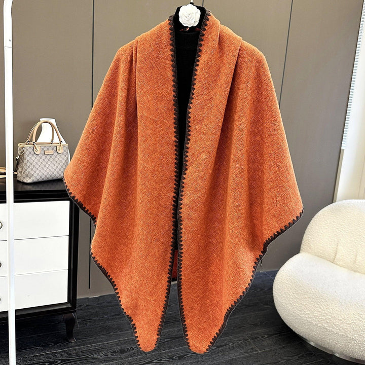 Orange woolen poncho with black trim displayed indoors near modern furniture and a designer handbag