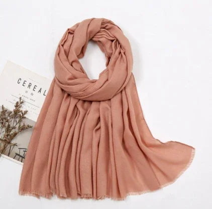 Soft blush pink scarf with fringed edges displayed on a white surface next to a magazine and dried flowers