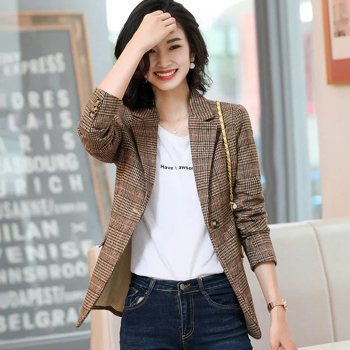Smiling woman wearing brown plaid blazer, white slogan t-shirt, and blue jeans indoors