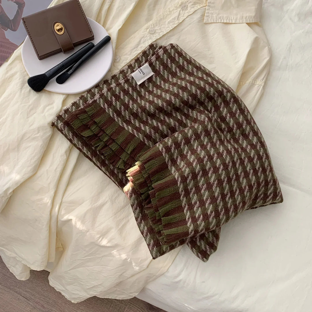 Folded brown and green houndstooth knit scarf on cream blouse with makeup brushes and brown wallet