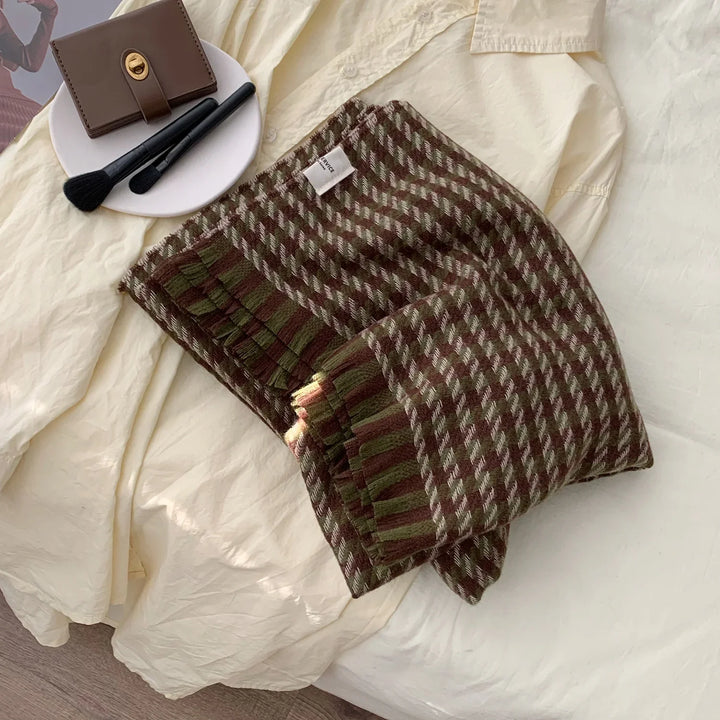 Folded brown and green houndstooth knit scarf on cream blouse with makeup brushes and brown wallet