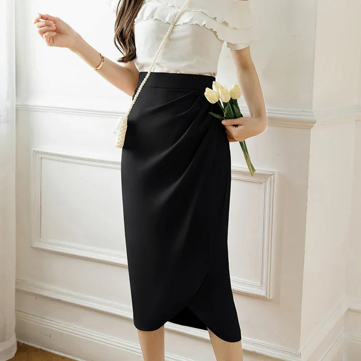 Woman wearing a black midi wrap skirt and white ruffle blouse holding white tulips indoors