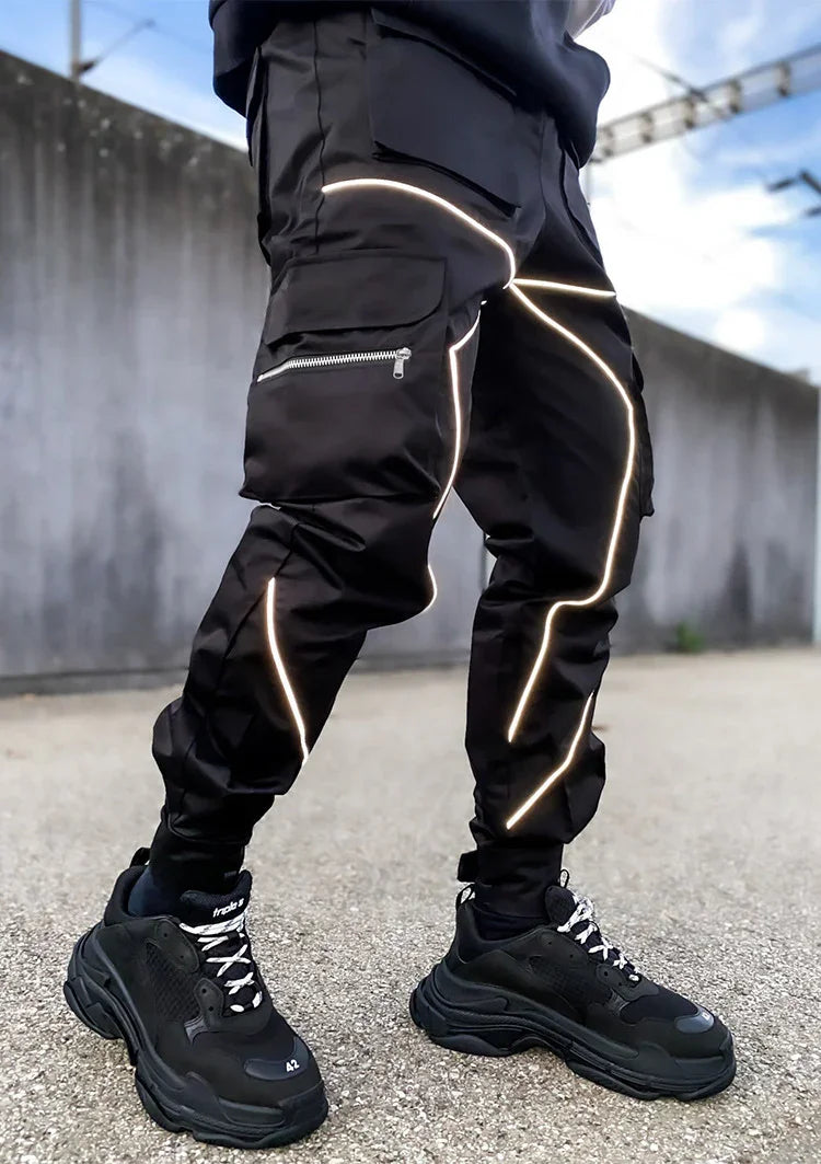 Black cargo pants with reflective piping and zippered pockets, paired with chunky black sneakers on asphalt