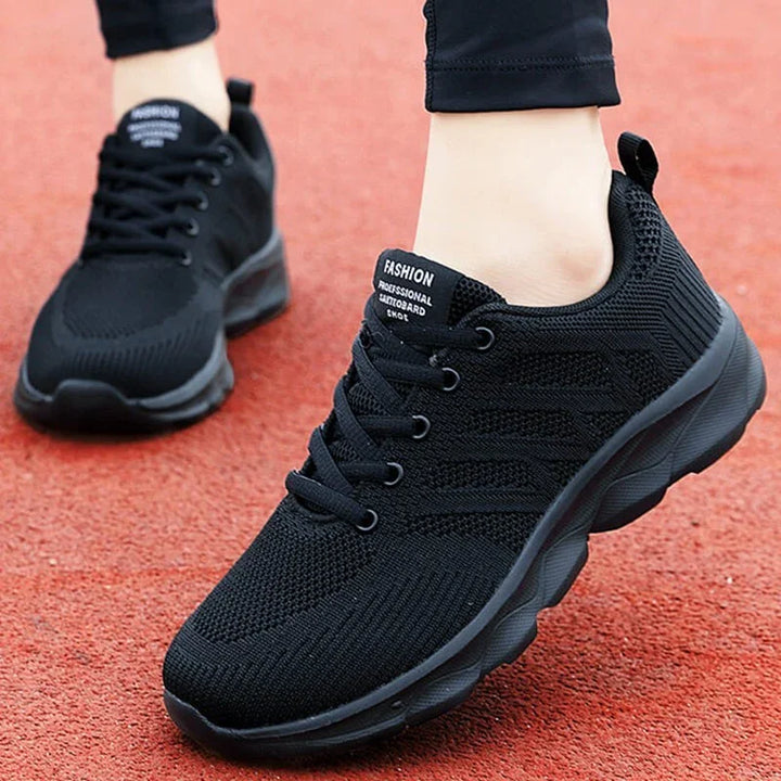 Black lightweight knit sneakers with lace-up design and cushioned sole on red track surface