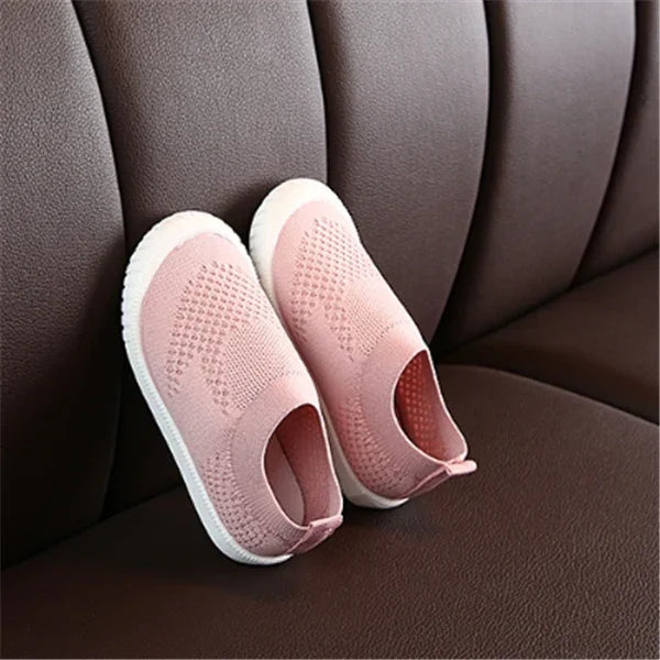 Pink knitted slip-on shoes with white soles on brown leather couch