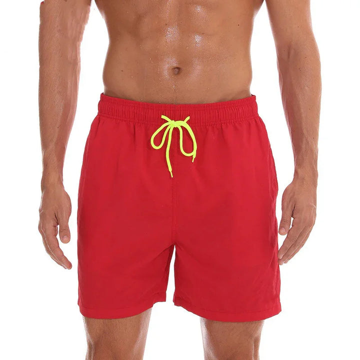 Man wearing red swim trunks with yellow drawstring, showing toned torso and arms on white background