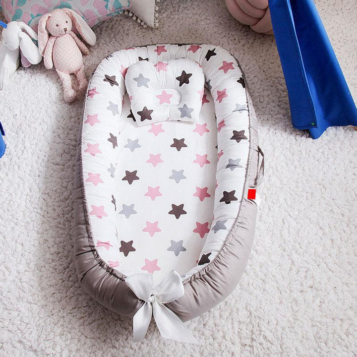 Baby nest with pink, grey, and brown star patterns and a small pillow on a plush carpet