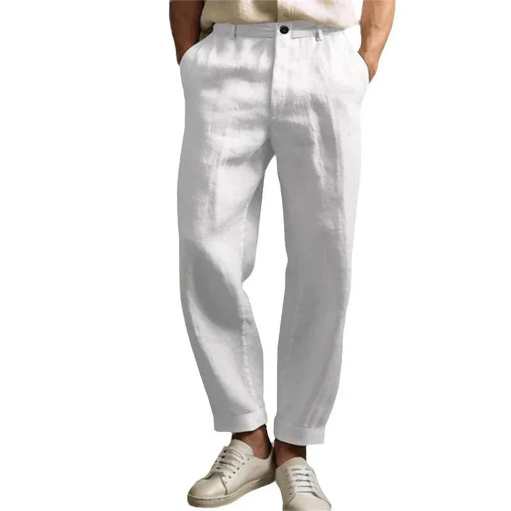 Men's white linen casual pants paired with beige sneakers, hands in pockets