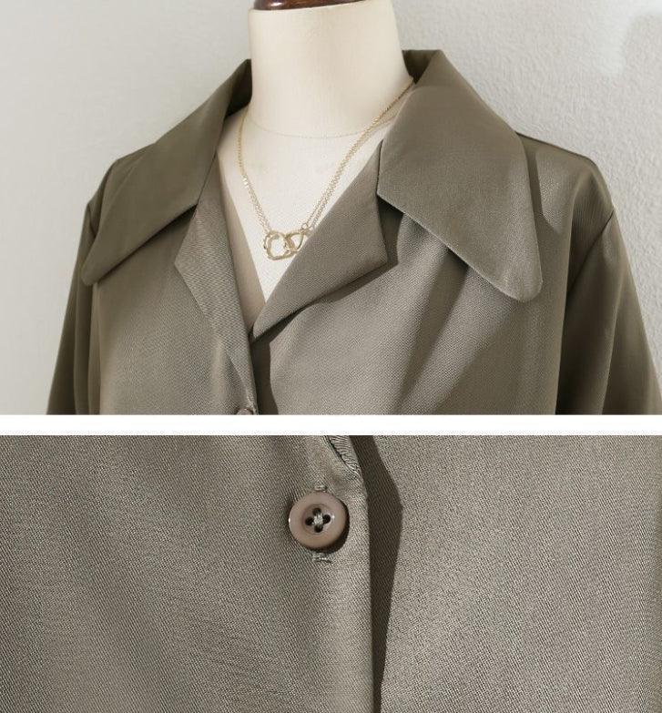 Close-up of olive green buttoned jacket on mannequin with wide collar and gold chain necklace