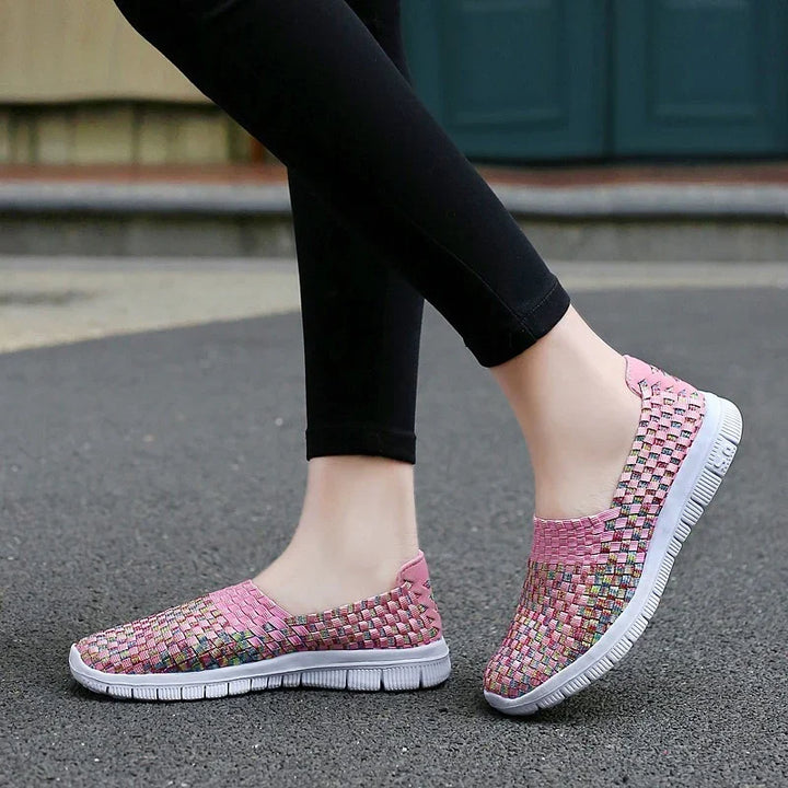 Pink woven slip-on sneakers with flexible white soles worn with black leggings on pavement