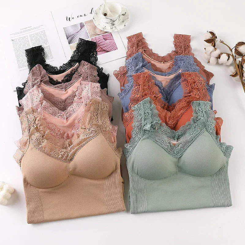 Stack of lace-trimmed seamless bras in various colors arranged on white surface with cotton stems and a cup