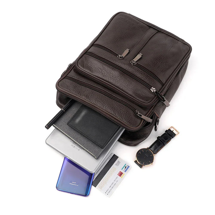 dark brown leather backpack with multiple zippered compartments and essentials like watch, cards, phone, tablet