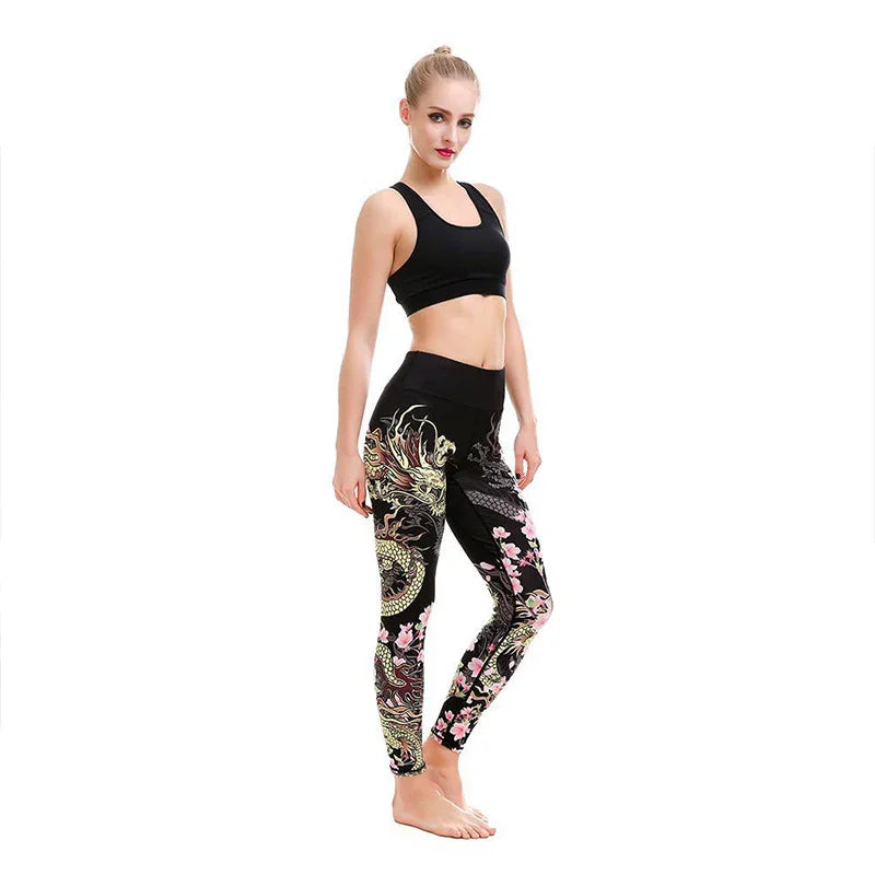 Woman wearing black sports bra and dragon floral print leggings, posing barefoot on white background