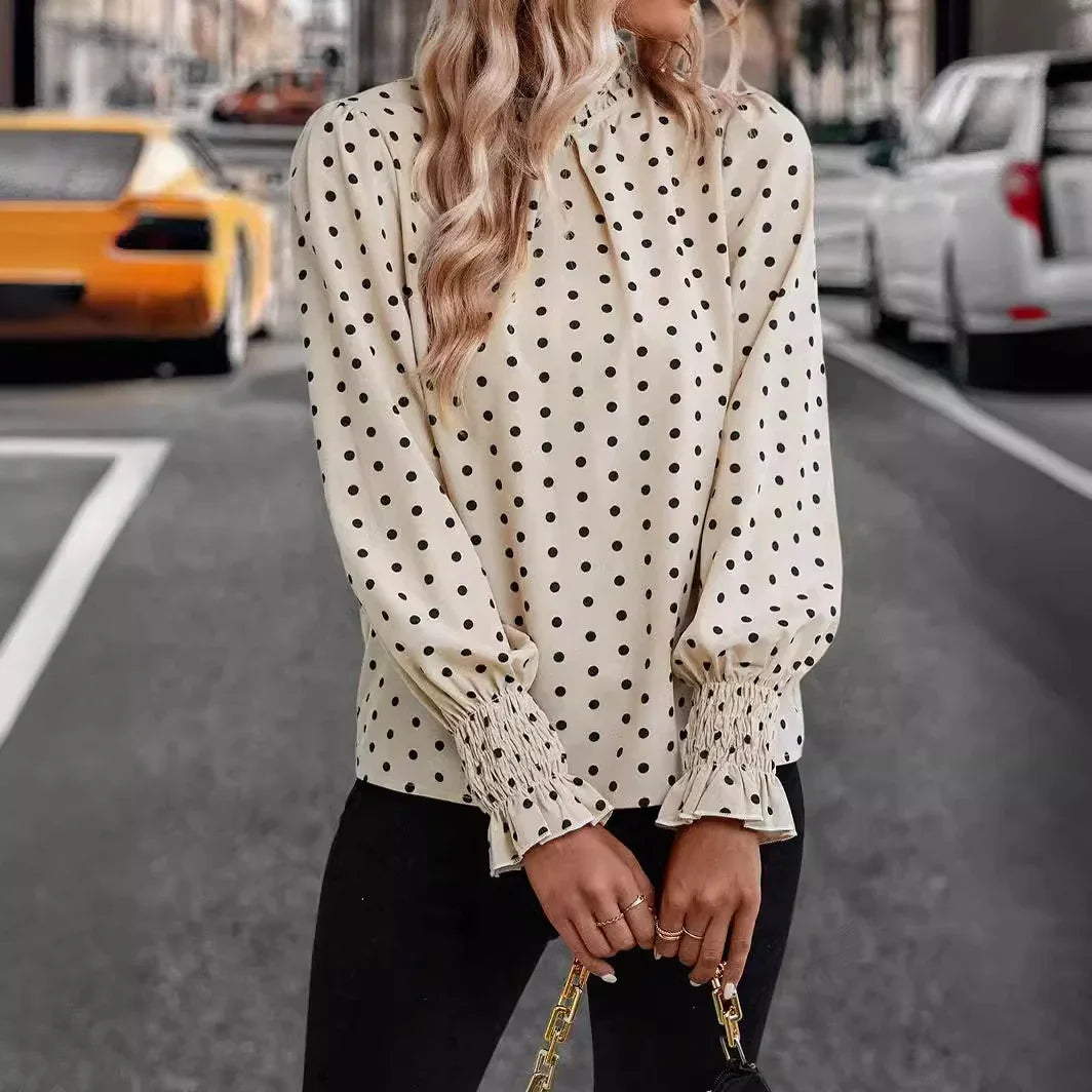 Woman wearing cream polka dot blouse with smocked cuffs and black pants holding a purse on city street