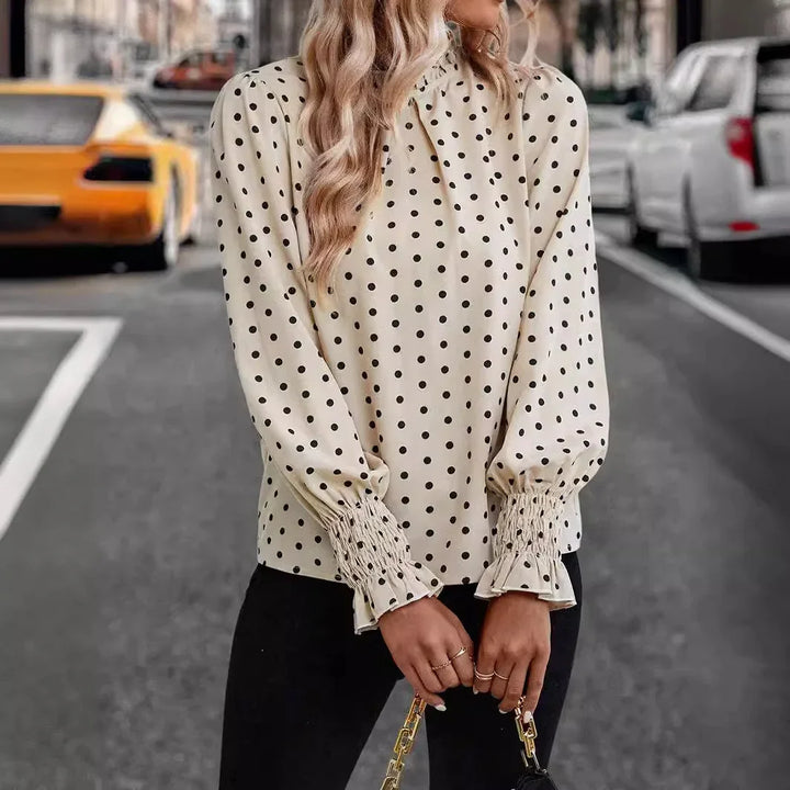 Woman wearing cream polka dot blouse with smocked cuffs and black pants holding a purse on city street