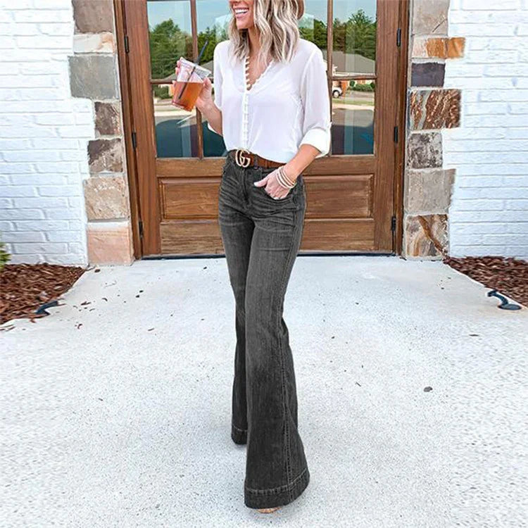 Woman wearing white blouse and black bell-bottom jeans standing outside wooden door with drink