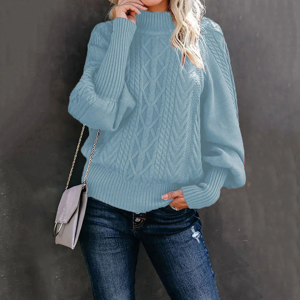 Woman wearing light blue cable knit sweater with puff sleeves and dark ripped jeans holding a gray purse