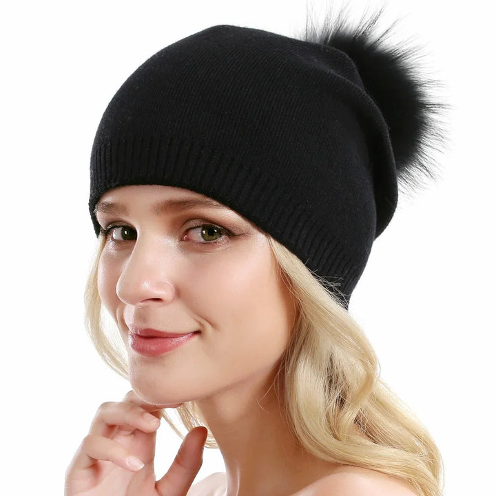 Young woman wearing a black knit beanie with a large fluffy pom pom on white background