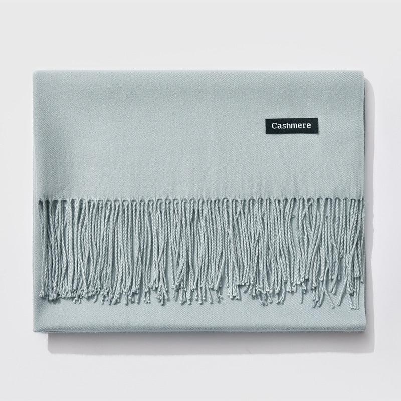 Light blue cashmere scarf with fringed edges folded neatly on white background