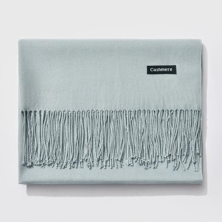 Light blue cashmere scarf with fringed edges folded neatly on white background