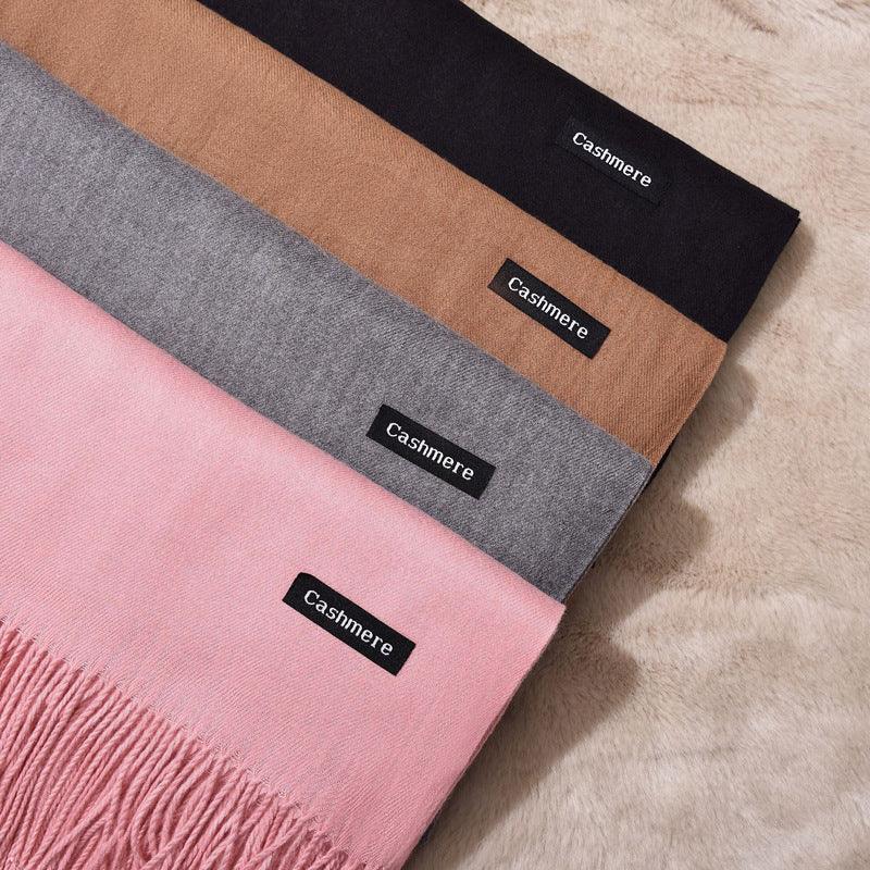 Four cashmere scarves in black, brown, grey, and pink with fringes, displayed on soft beige fabric