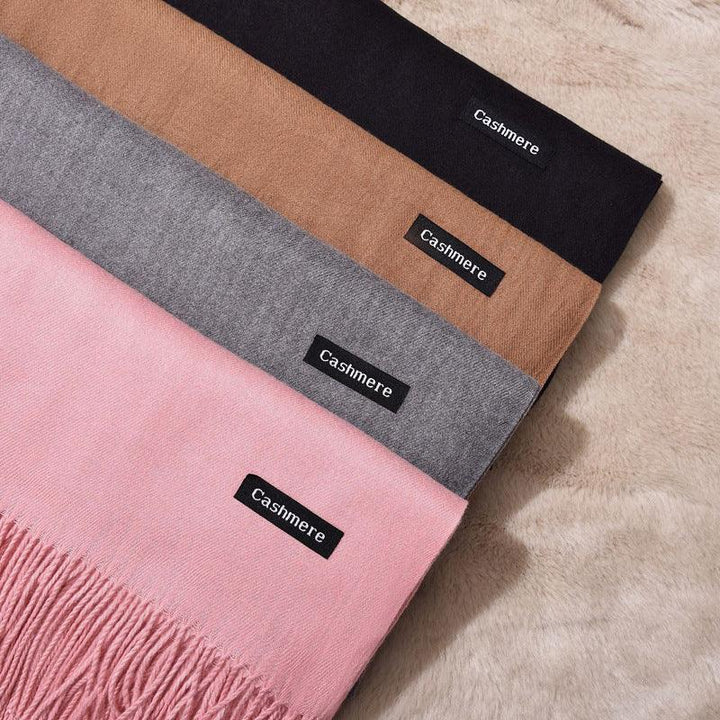 Four cashmere scarves in black, brown, grey, and pink with fringes, displayed on soft beige fabric