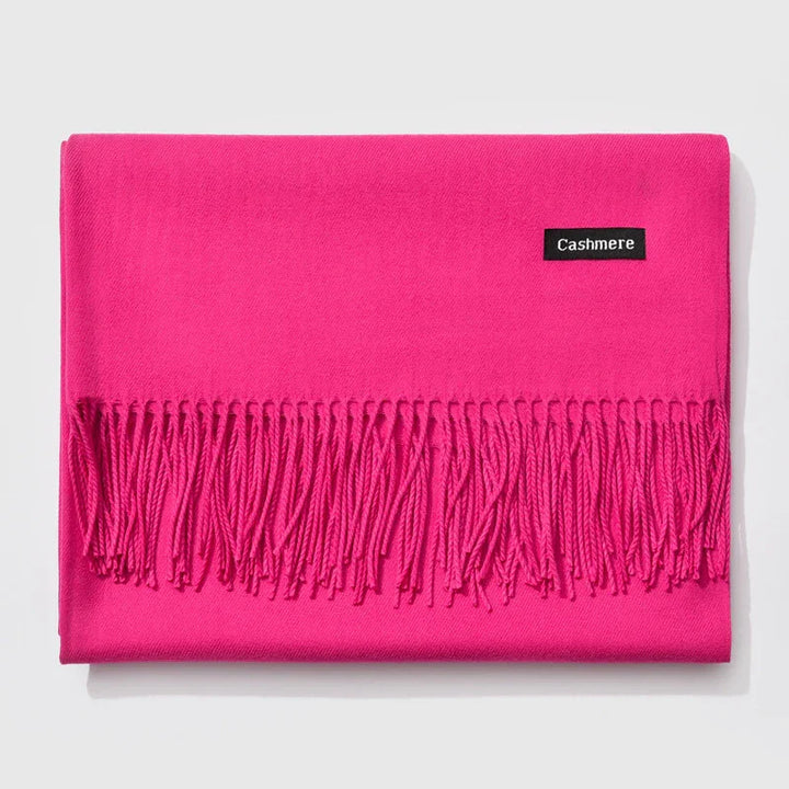 Bright pink cashmere scarf with fringed edges folded on a white background