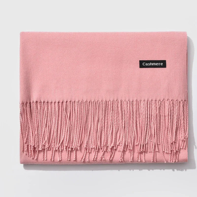 Soft pink cashmere scarf with fringed ends neatly folded on white background